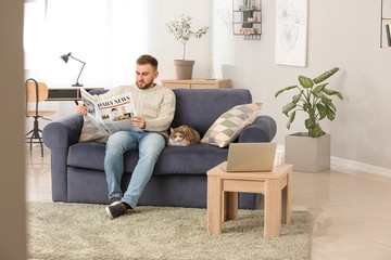 Obraz premium Man with cute cat reading newspaper at home