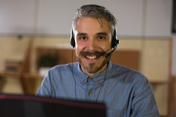 Smiling call center operator looking at camera. Handsome bearded man working with laptop in office....