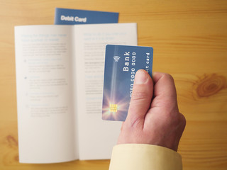 Man holding brand new debit card in his hand, Blurred terms and conditions booklet in the background, top view. Concept banking documents and service.