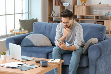 Fototapeta premium Confused young man with mobile phone at home