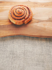 One traditional freshly cooked cinnamon swirl, pastry product on a wooden board surface and simple table cloth. Close up.