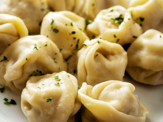 Portion of traditional Russian cooked dumplings with herb on a white plate.