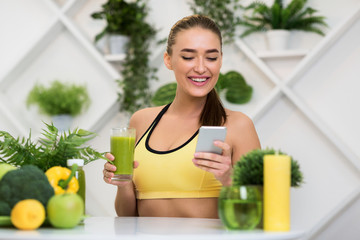 Happy woman using phone and drinking green smoothie juice