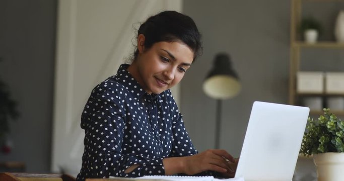 Smiling indian girl student typing on laptop preparing course work