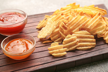 Tasty potato chips and sauces on wooden board