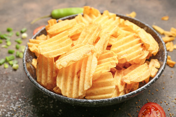 Plate with tasty potato chips on grunge background