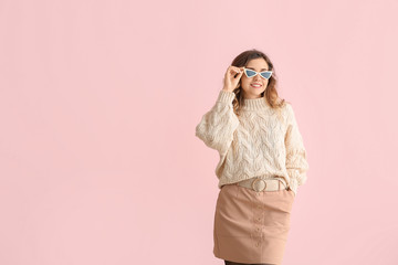 Beautiful young woman in warm sweater on color background