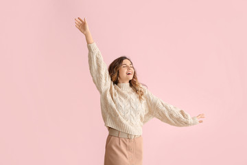 Beautiful young woman in warm sweater on color background