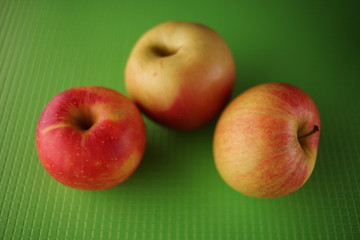 three ripe apples, red with yellow color, lie on a green table.