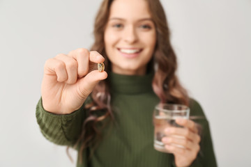 Young woman with fish oil on light background, closeup