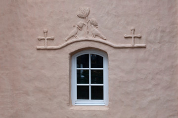 Fragment of the wall of an old church with a window decorated with a bas-relief in the form of two birds