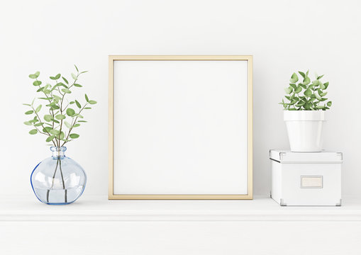 Interior poster mockup with square gold metal frame on the table with plants in blue vase, pot and box on empty white wall background. 3D rendering, illustration.