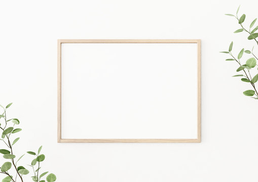 Interior poster mockup with horizontal wooden frame on empty white wall, decorated with plant branches with green leaves. A4, A3 size format. 3D rendering, illustration.
