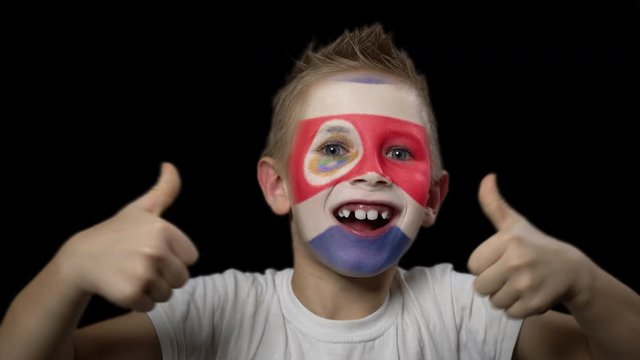 Happy boy rejoices victory of his favorite team of Costa Rica. A child with a face painted in national colors. Portrait of a happy young fan. Joyful emotions and gestures. Victory. Triumph.