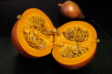 Pumpkin cut in half showing the seeds and pulp inside with a onion in the background, selected focus