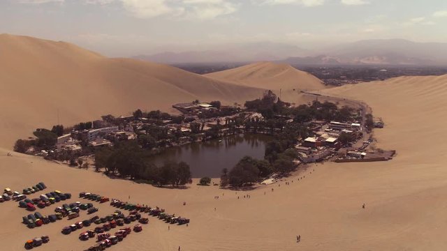 Sandy desert oasis lake. DRONE.  Tourism shot in Huacachina, Peru. Water in middle of hot sand desert. Adventure Dune Buggy, Speed. Epic, Fast. Romantic, holiday, honeymoon, scenic shot.