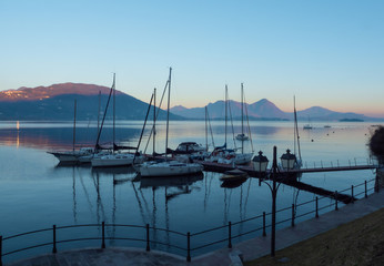 the soft colors of the sky reflected on the calm water of a small port at sunset on Lake Maggiore