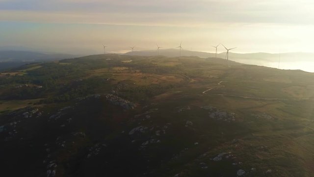 Drone footage of rotating windmills on top of hill near Playa de Barizo in As Garzas, Spain during a beautiful warm golden hour sunset
