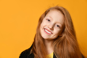 Red-haired teenage kid in black jacket. She is smiling and looking at you, posing against orange studio background. Close up