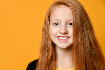 Red-haired teenage kid in black jacket. She is smiling and looking at you, posing against orange studio background. Close up