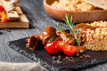 Eastern cuisine. A modern serving of pilaf in a restaurant on black slate, meat lies nearby.
