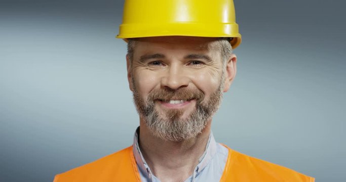 Close up of the happy Caucasian man constructor and designer in the yellow helmet smiling to the camera cheerfully. Portrait.
