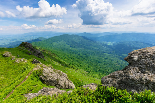 mountain landscape in summer. view from the top of carpathian watershed ridge in to the distance. boulders on the green grassy slopes. sunny weather with clouds on the blue sky