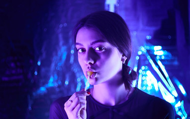 beautiful girl with a lollipop in her mouth cute looking at camera. neon lamps. model posing.    