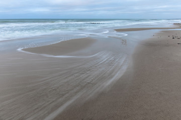 landscape of wide sandy beach by the cold Baltic sea in cloudy weather at long exposure