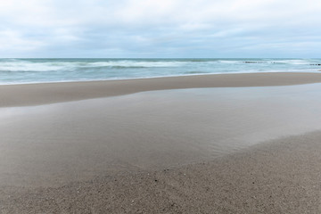 landscape of wide sandy beach by the cold Baltic sea in cloudy weather at long exposure