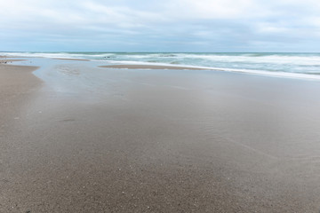 landscape of wide sandy beach by the cold Baltic sea in cloudy weather at long exposure