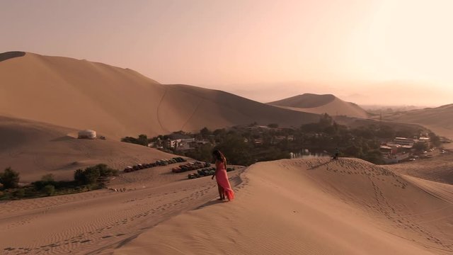 Woman in Sandy desert oasis lake. DRONE. Tourism shot in Huacachina, Peru. Romantic, holiday, honeymoon, scenic shot.Water in middle of hot sand desert. Adventure Dune Buggy, Speed. Epic, Fast. 