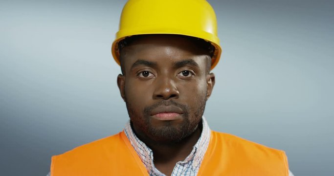 Close up of the young African American male builder or designer in the yellow helmet looking at the camera. Portrait.
