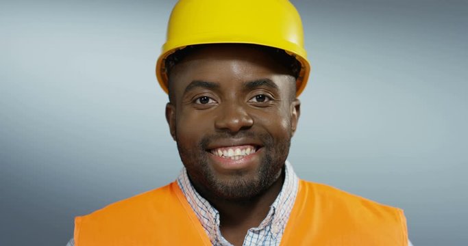 Portrait of the happy and cheerful African American young man builder and constructor in a yellow casque smiling to the camera. Close up.