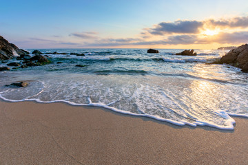 sunrise on the beach. beautiful summer scenery. rocks on the sand. calm waves on the water. clouds on the sky. wide panoramic view