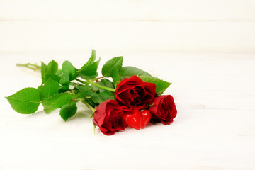 three red roses and a two heart shapes from glass on a white wooden background, love concept with copy space