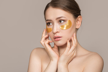 Portrait of a young beautiful woman with natural make-up. Gold collagen spots on fresh skin. The concept of skin care around the eyes. Copycpase