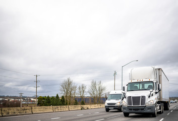 Fototapeta na wymiar Big rig semi truck with dry van semi trailer driving on the road beside the commercial cargo mini van