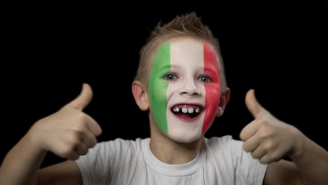 Happy boy rejoices victory of his favorite team of Italy. A child with a face painted in national colors. Portrait of a happy young fan. Joyful emotions and gestures. Victory. Triumph.