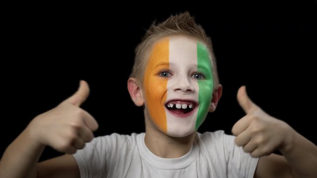 Happy boy rejoices victory of his favorite team of the Ivory Coast. A child with a face painted in national colors. Portrait of a happy young fan. Joyful emotions and gestures. Victory. Triumph.