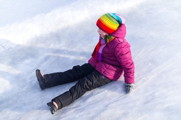 Fototapeta na wymiar Child rolls down an ice slide. Bright clothes rainbow hat.