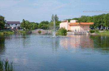 Russia, Blagoveshchensk, July 2019: fountain on pond and orange building in friendship Park in Blagoveshchensk in summer