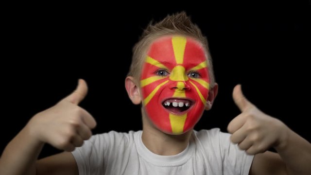 Happy boy rejoices victory of his favorite team of Macedonia. A child with a face painted in national colors. Portrait of a happy young fan. Joyful emotions and gestures. Victory. Triumph.