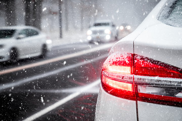 Rear red tail light on white car stopped on road during a snow storm