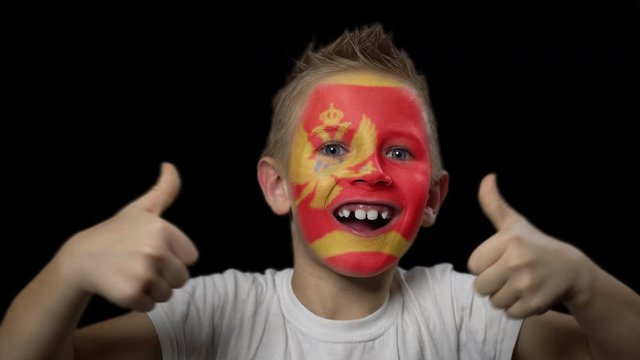 Happy boy rejoices victory of his favorite team of Montenegro. A child with a face painted in national colors. Portrait of a happy young fan. Joyful emotions and gestures. Victory. Triumph.