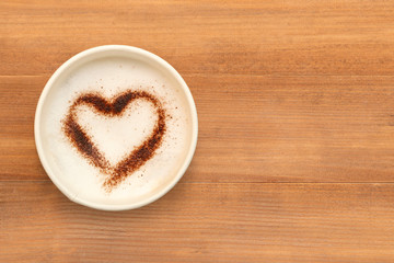 Top view of cup of cappuccino coffee with  heart shaped chocolate powder on brown wooden table