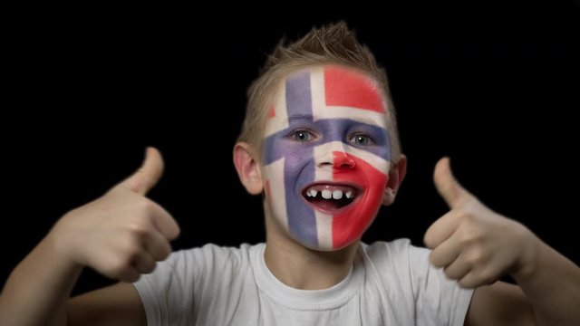 Happy boy rejoices victory of his favorite team of Norway. A child with a face painted in national colors. Portrait of a happy young fan. Joyful emotions and gestures. Victory. Triumph.