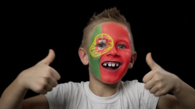 Happy boy rejoices victory of his favorite team of Portugal. A child with a face painted in national colors. Portrait of a happy young fan. Joyful emotions and gestures. Victory. Triumph.