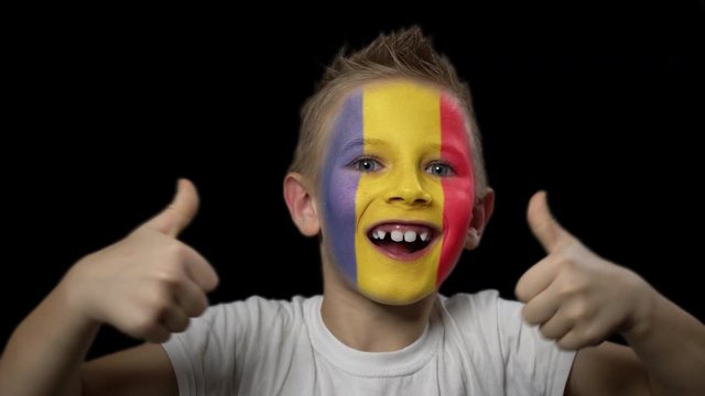Happy boy rejoices victory of his favorite team of Romania. A child with a face painted in national colors. Portrait of a happy young fan. Joyful emotions and gestures. Victory. Triumph.