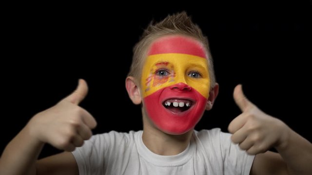 Happy boy rejoices victory of his favorite team of Spain. A child with a face painted in national colors. Portrait of a happy young fan. Joyful emotions and gestures. Victory. Triumph.